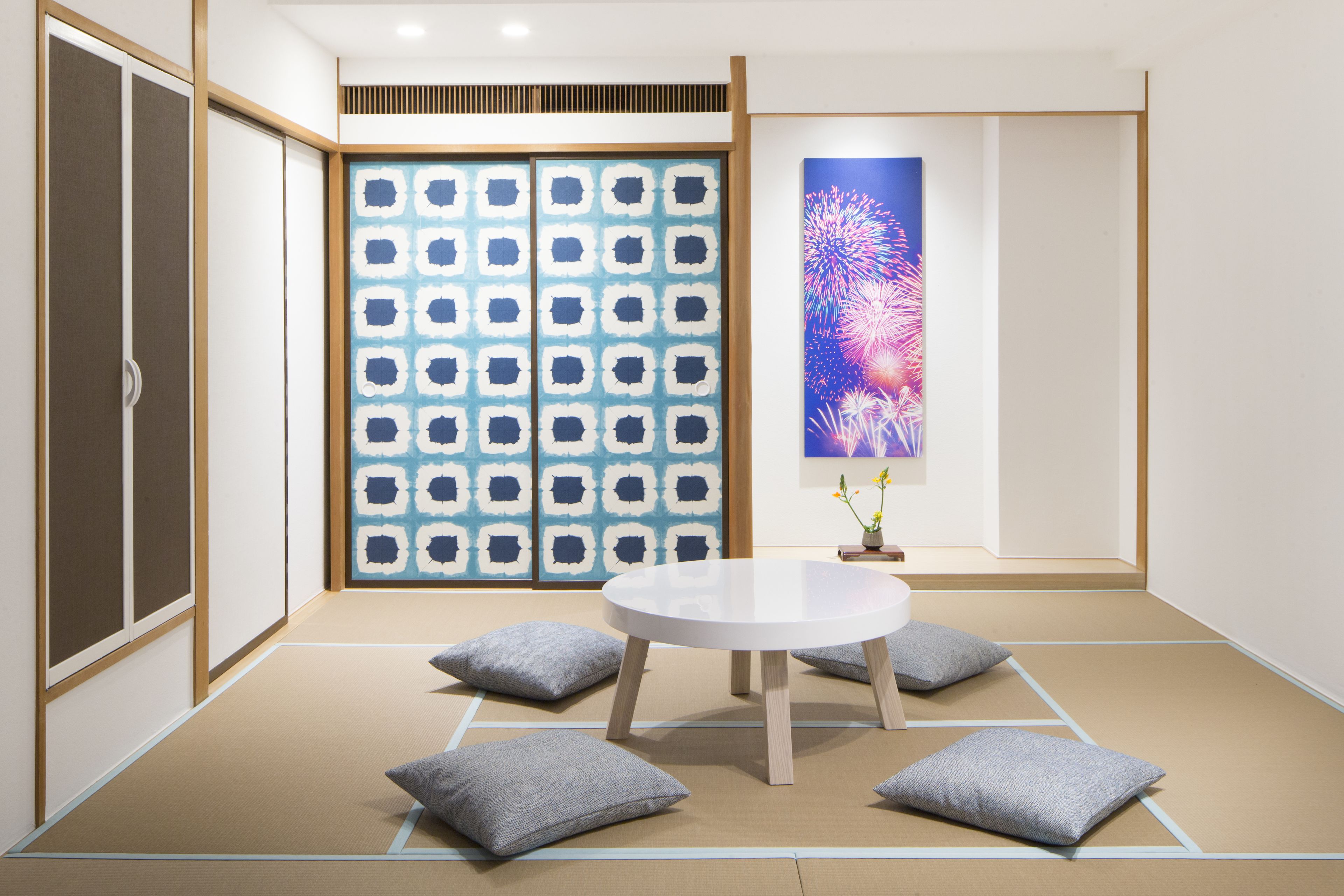 A traditional Japanese room with tatami flooring, a low wooden table, cushions, and a sliding door with a geometric pattern.