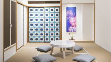 A traditional Japanese room with tatami flooring, a low wooden table, cushions, and a sliding door with a geometric pattern.