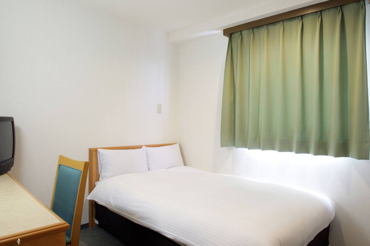 A hotel room with a single bed, a desk, and a television.
