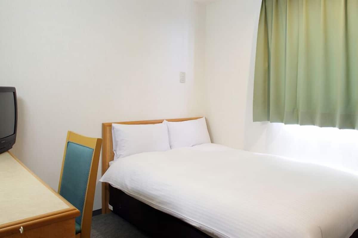 A hotel room with a bed, a desk, a television, and a window with curtains.