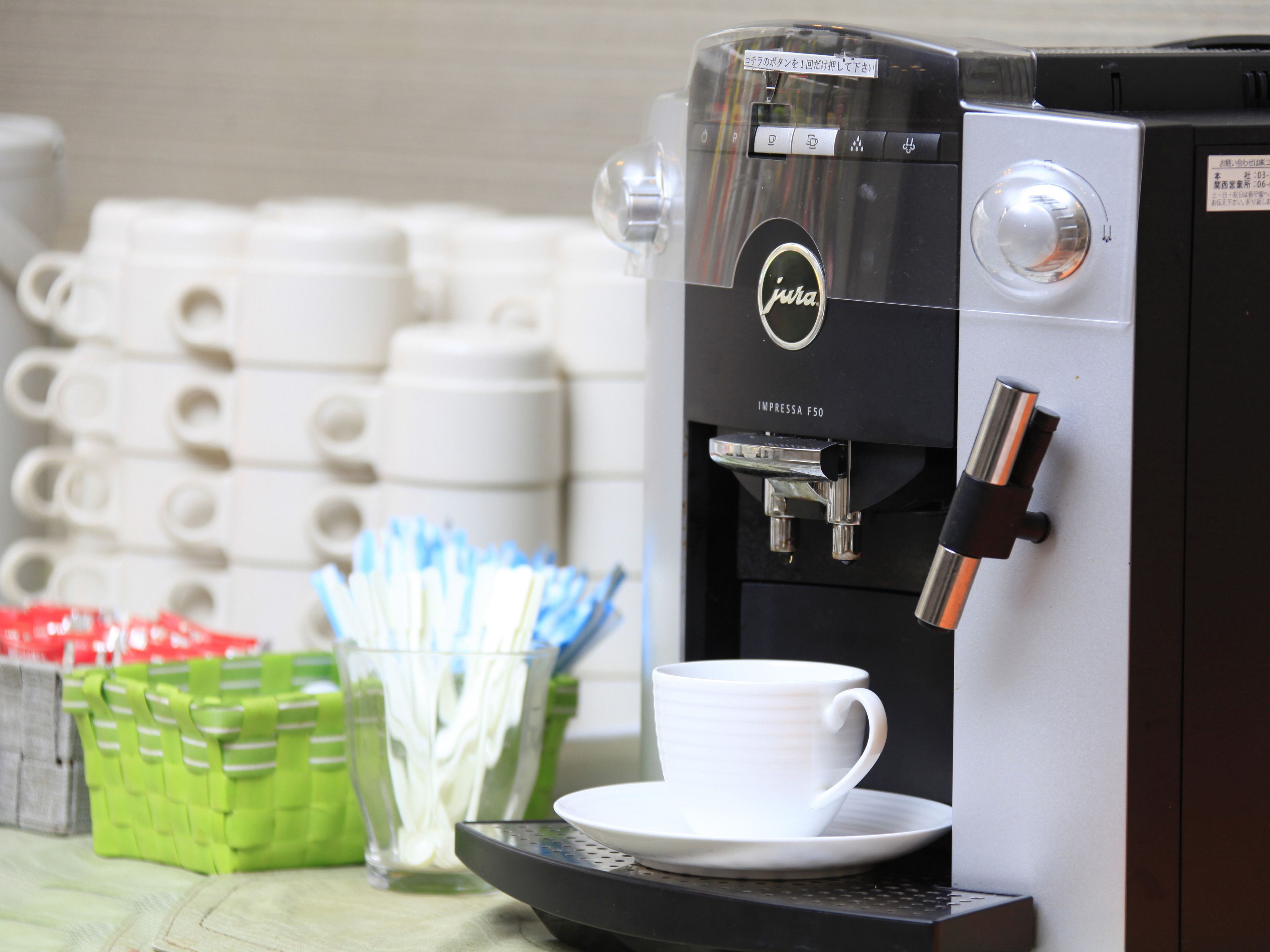 A coffee machine with a cup and saucer, disposable cups, and green containers.