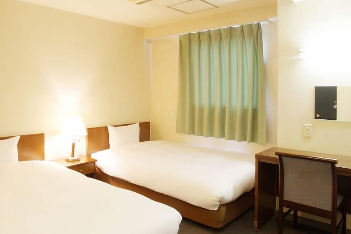 A hotel room with two beds, a desk, and a chair.