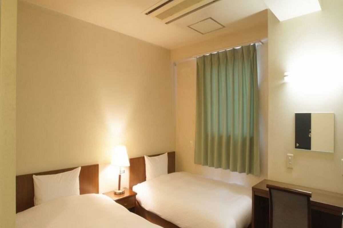 A hotel room with two beds, a desk, a chair, a lamp, and a window with curtains.