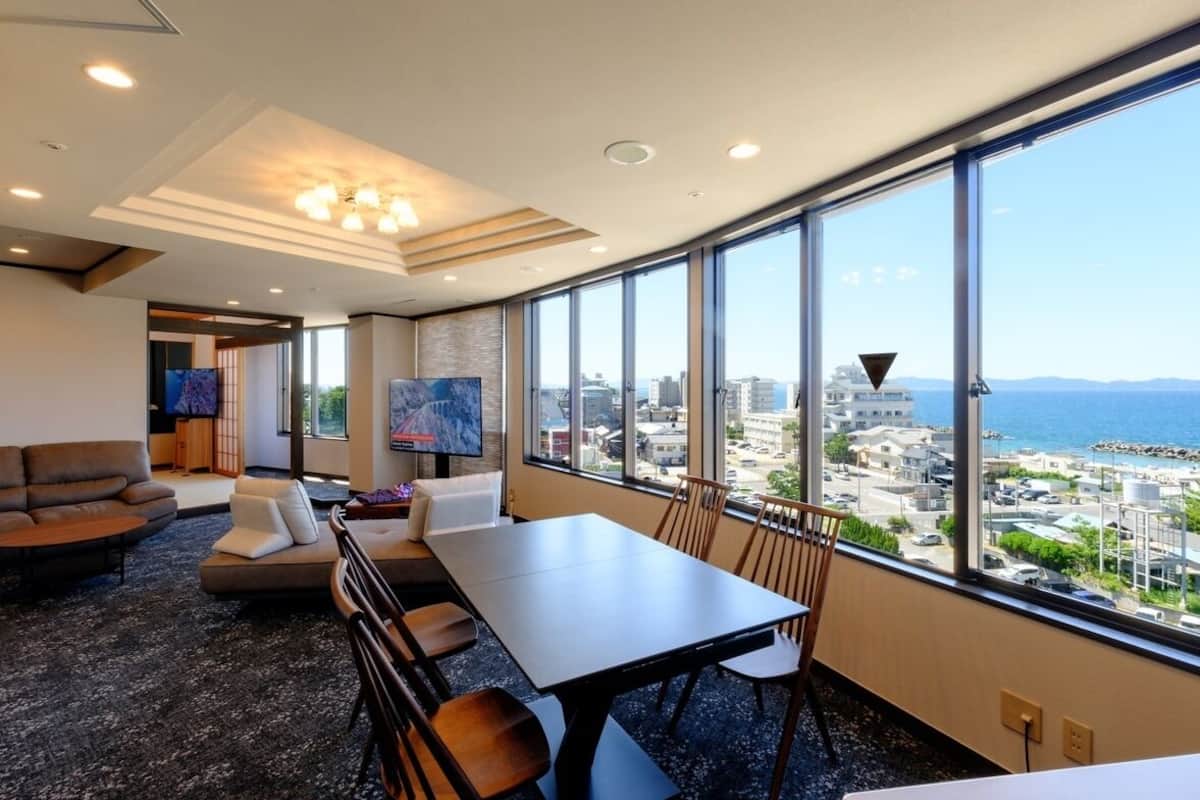A modern hotel room with a large window, a dining area, and a seating area.