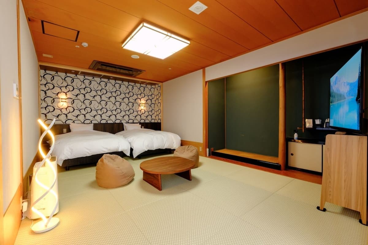 A hotel room with two beds, a TV, a desk, and a large window.