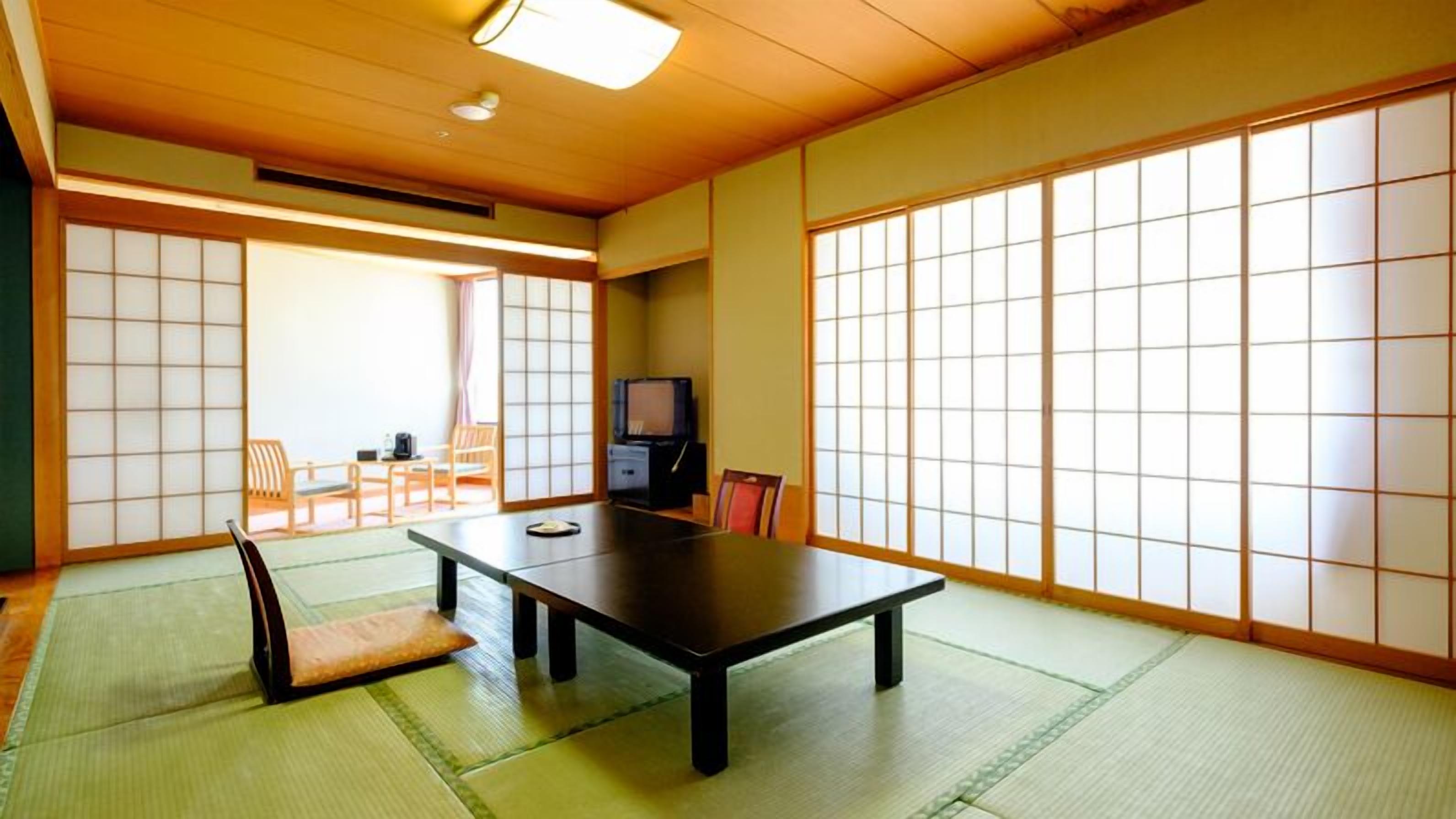 A traditional Japanese room with tatami flooring, a low table, sliding doors, and a television.