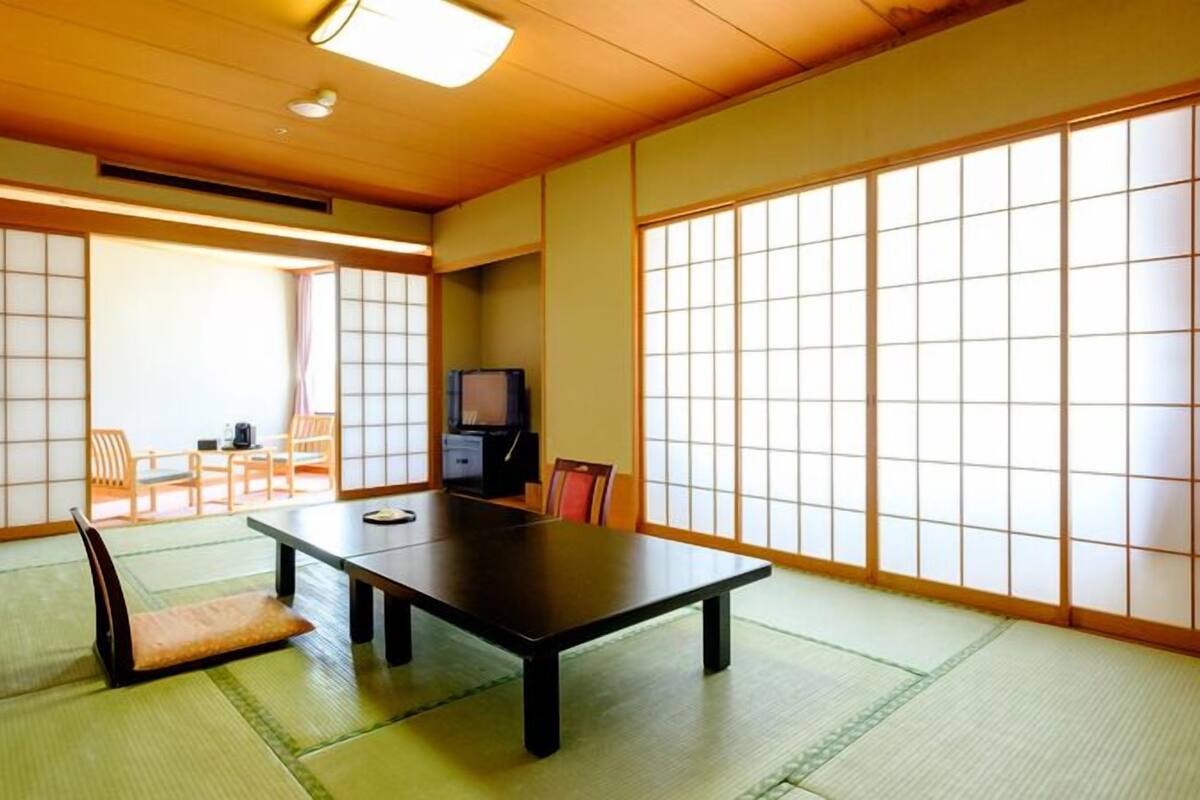 A traditional Japanese room with tatami flooring, a low table, sliding doors, and a television.