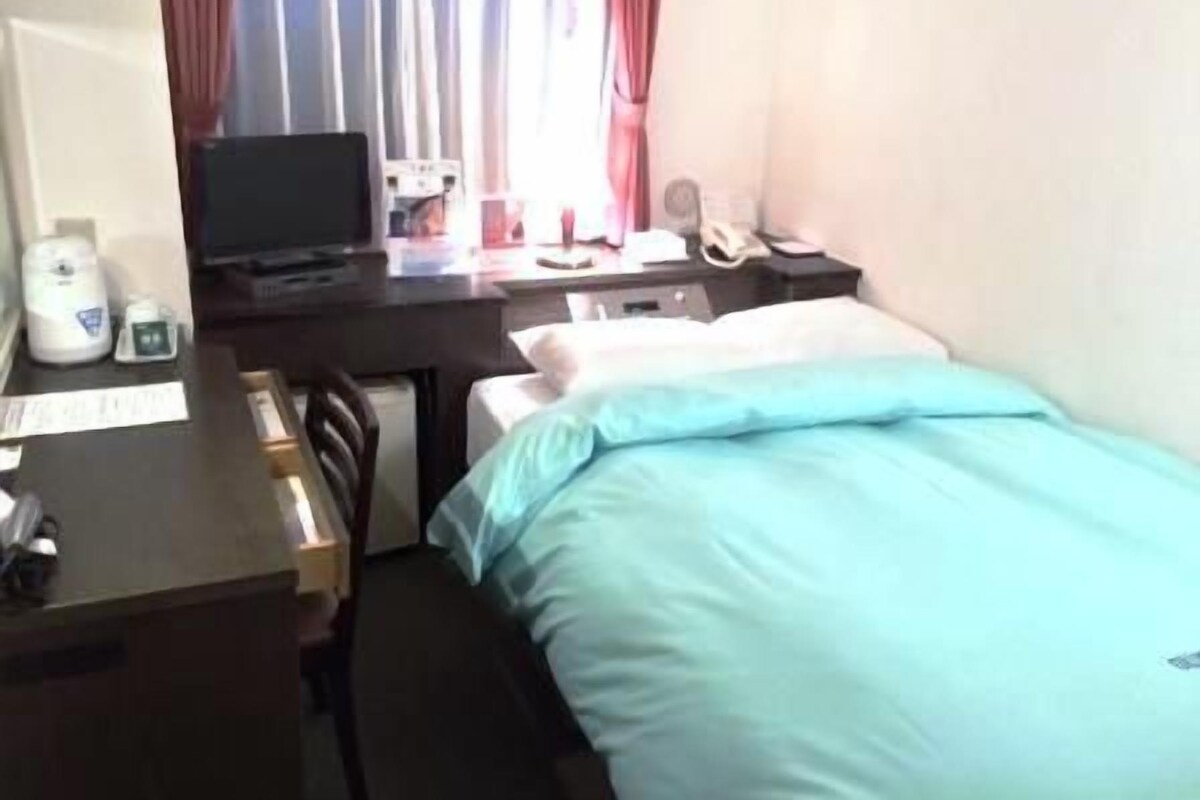 Une chambre d’hôtel avec un lit, un bureau, une chaise et une fenêtre avec des rideaux.
