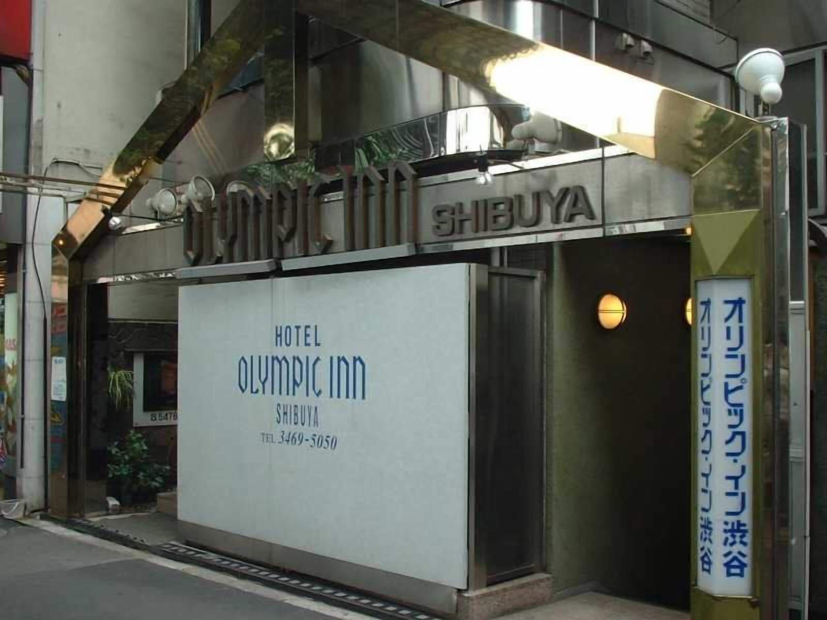 L’entrée d’un hôtel, avec une enseigne indiquant « Hôtel Olympic Inn » et un numéro de téléphone.