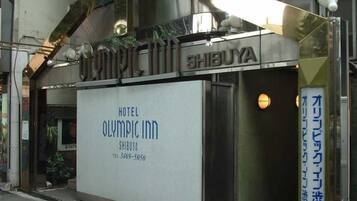 L’entrée d’un hôtel, avec une enseigne indiquant « Hôtel Olympic Inn » et un numéro de téléphone.