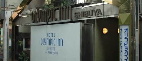 L’entrée d’un hôtel, avec une enseigne indiquant « Hôtel Olympic Inn » et un numéro de téléphone.