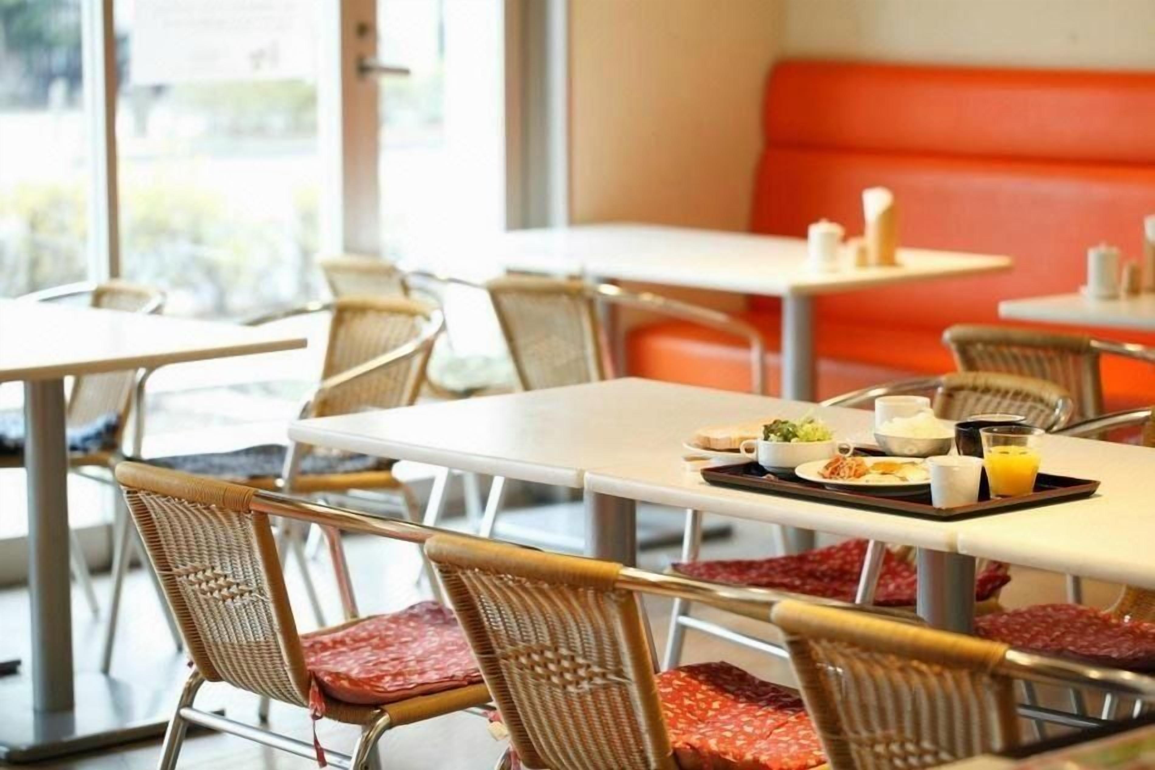 A dining area with tables and wicker chairs, some with red cushions.