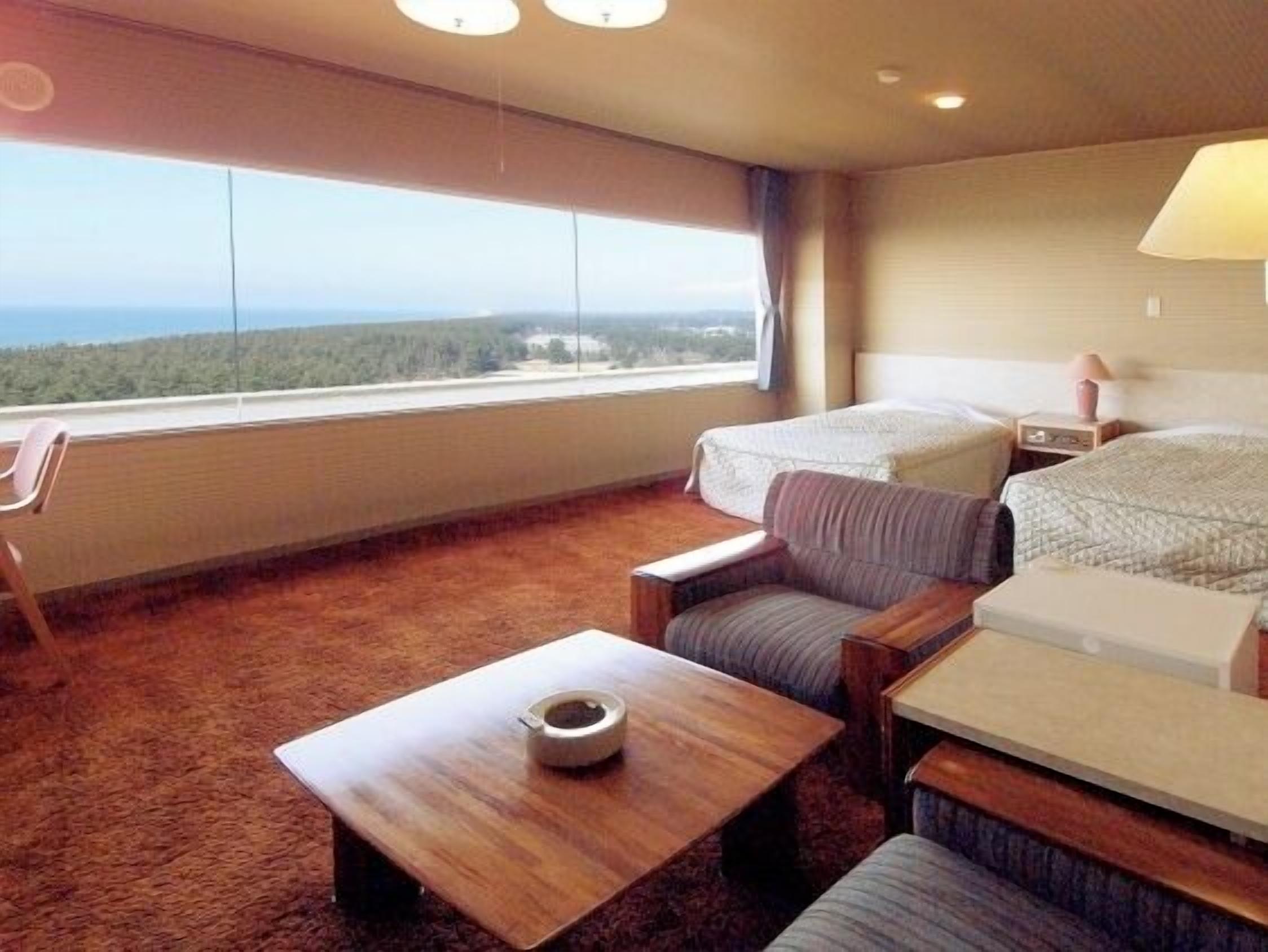 A hotel room with a large window, a bed, a sofa, a small table, and a chair.