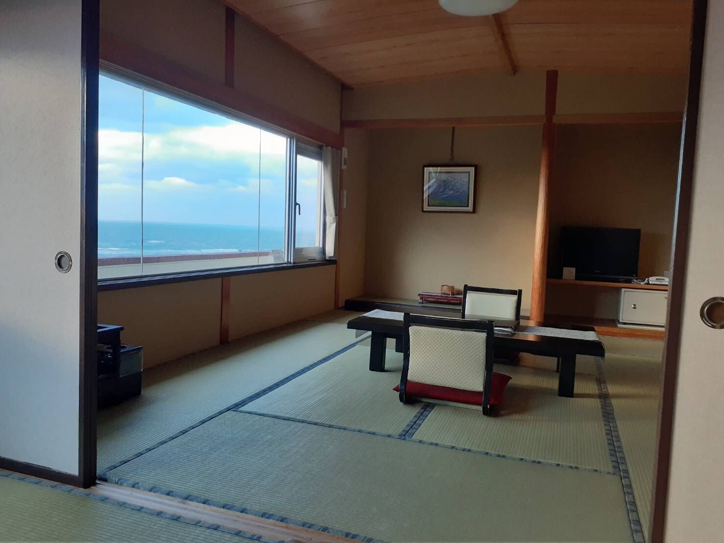 A room with tatami flooring, a low table with chairs, a television, and a painting on the wall.