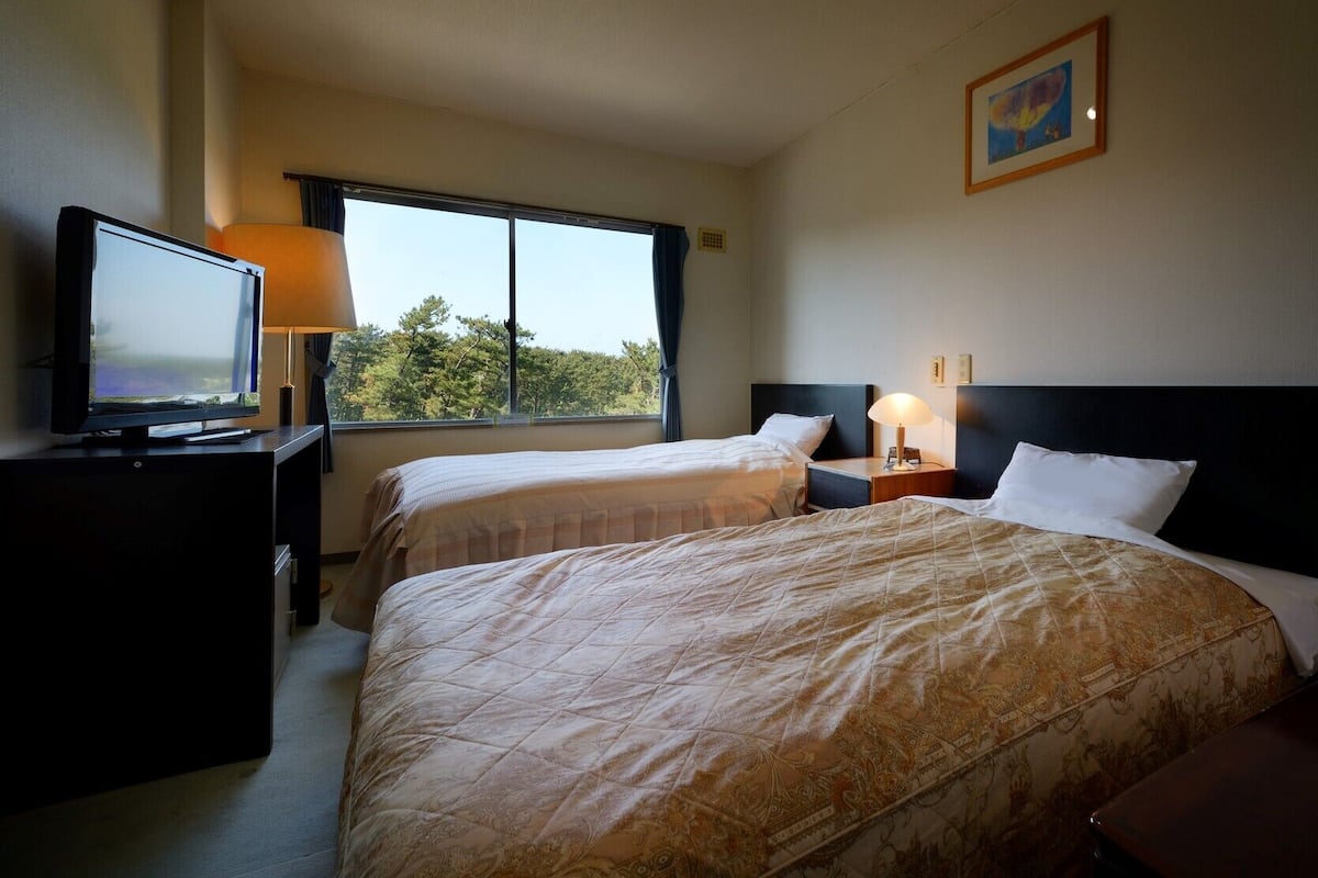A hotel room with two beds, a TV, a window with a view, and a painting on the wall.