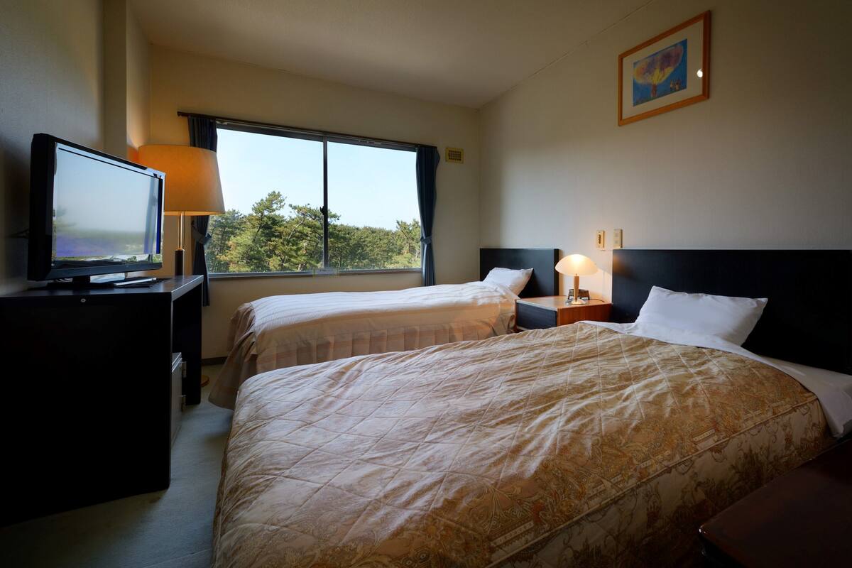 A hotel room with two beds, a television, a window with a view of trees, and a painting on the wall.