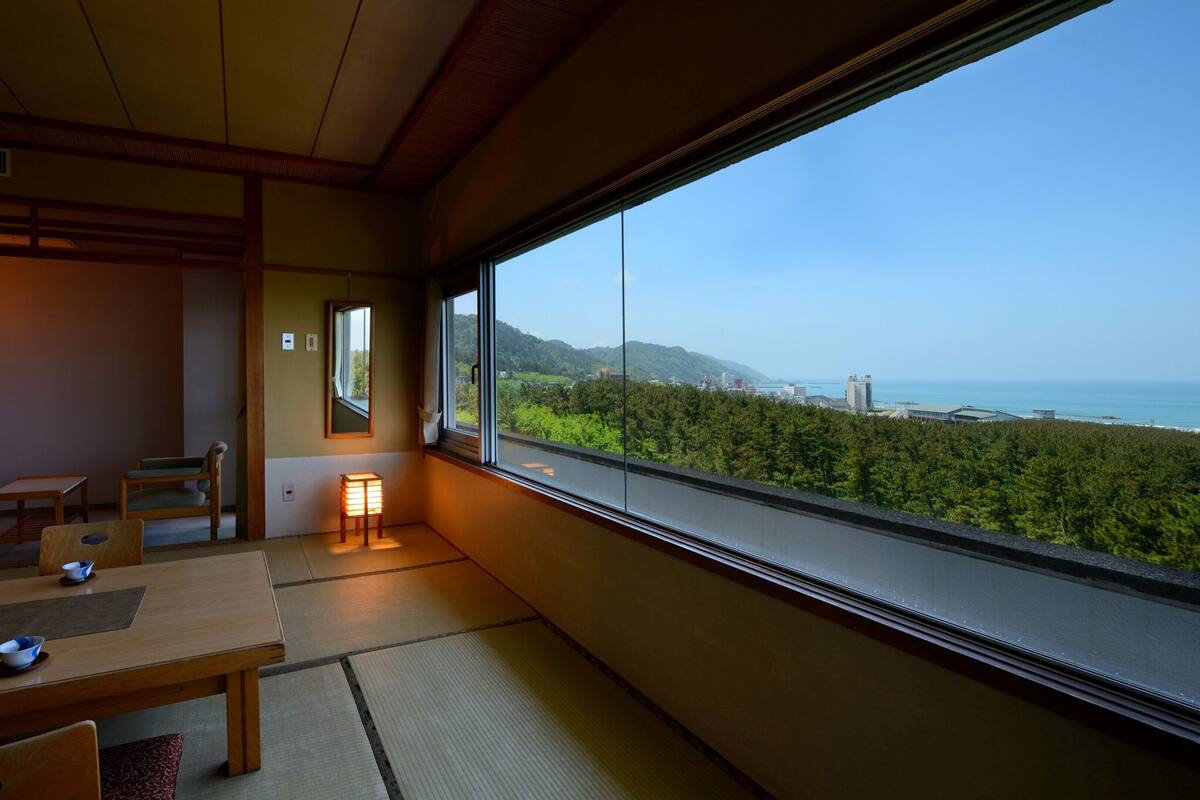 A room with tatami flooring, a low table with a bowl, and a view of a coastal landscape.