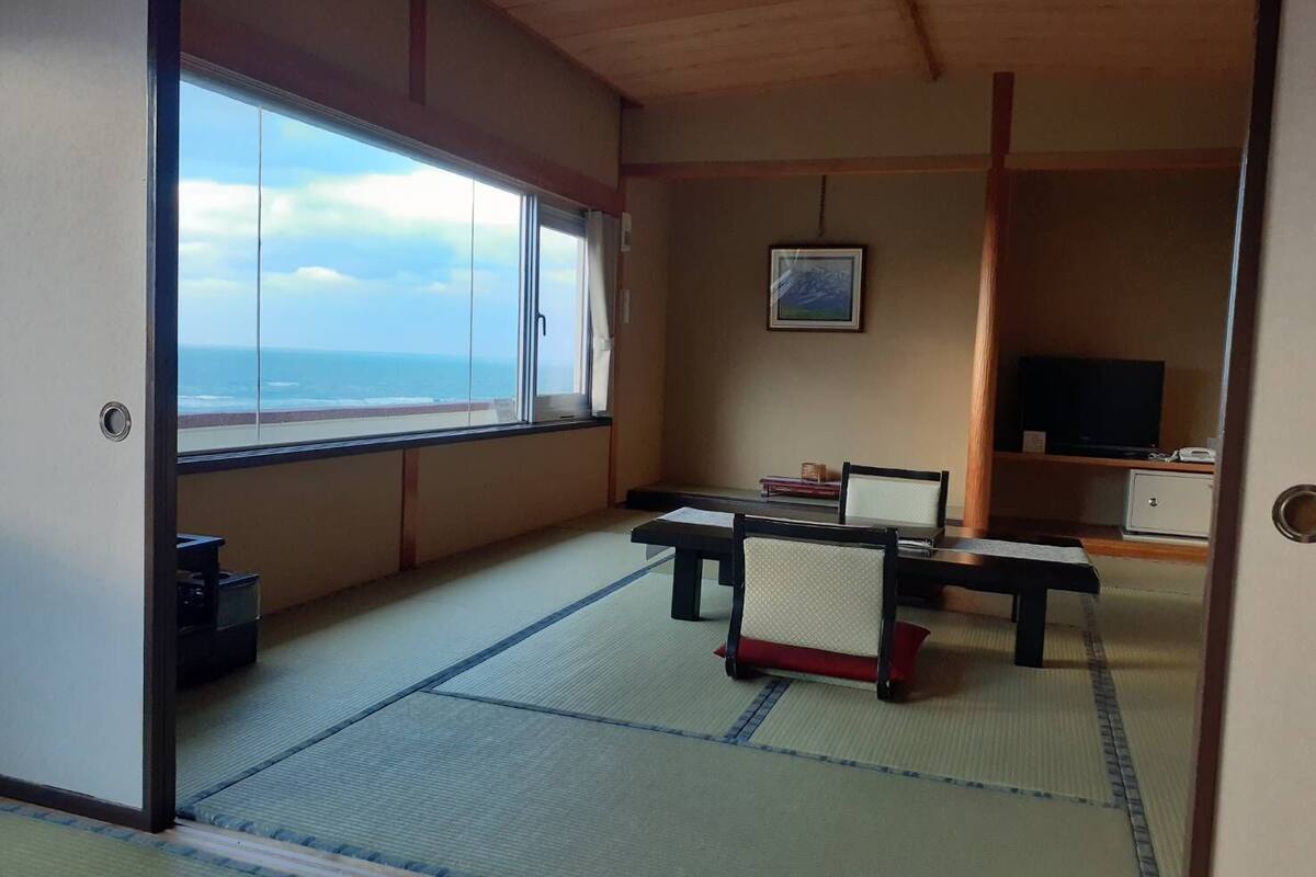 A room with tatami flooring, a low table with chairs, a television, and a framed picture on the wall.