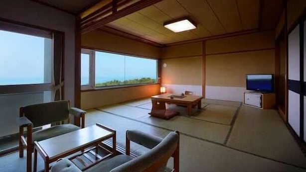 A traditional Japanese-style room with tatami flooring, a low table, a sofa, and a television. - Hanayubi Nihonkai (Tsuruoka)