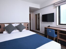 Una habitación de hotel con cama, escritorio, silla, televisor y armario.