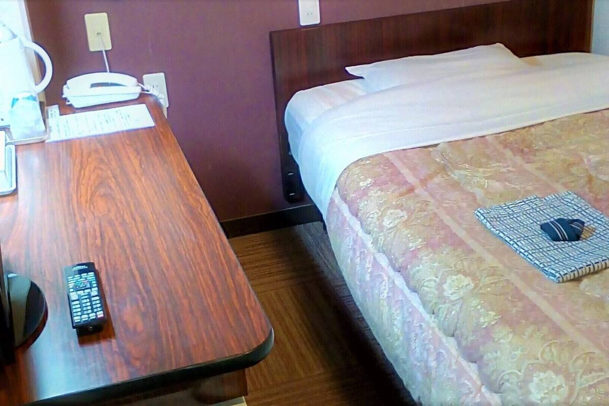 Una habitación de hotel con un escritorio de madera, una cama con colcha estampada, un control remoto y una libreta doblada.