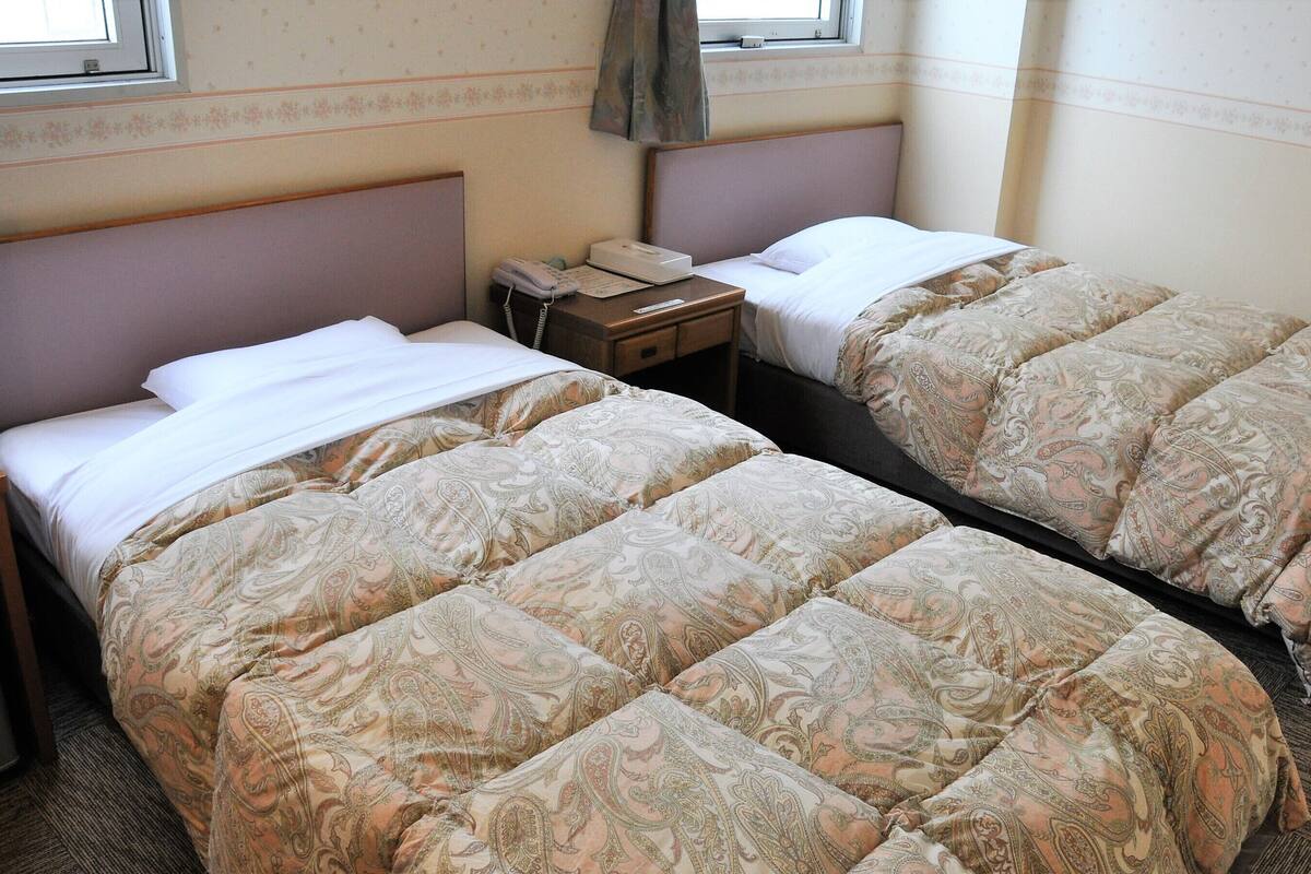 Una habitación de hotel con dos camas, una mesita de noche con teléfono y una ventana con cortinas.