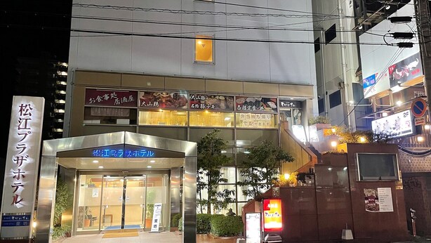 A hotel entrance with a blue sign, multiple floors, and various restaurant signs above. - Matsue Plaza Hotel Honkan (Matsue)