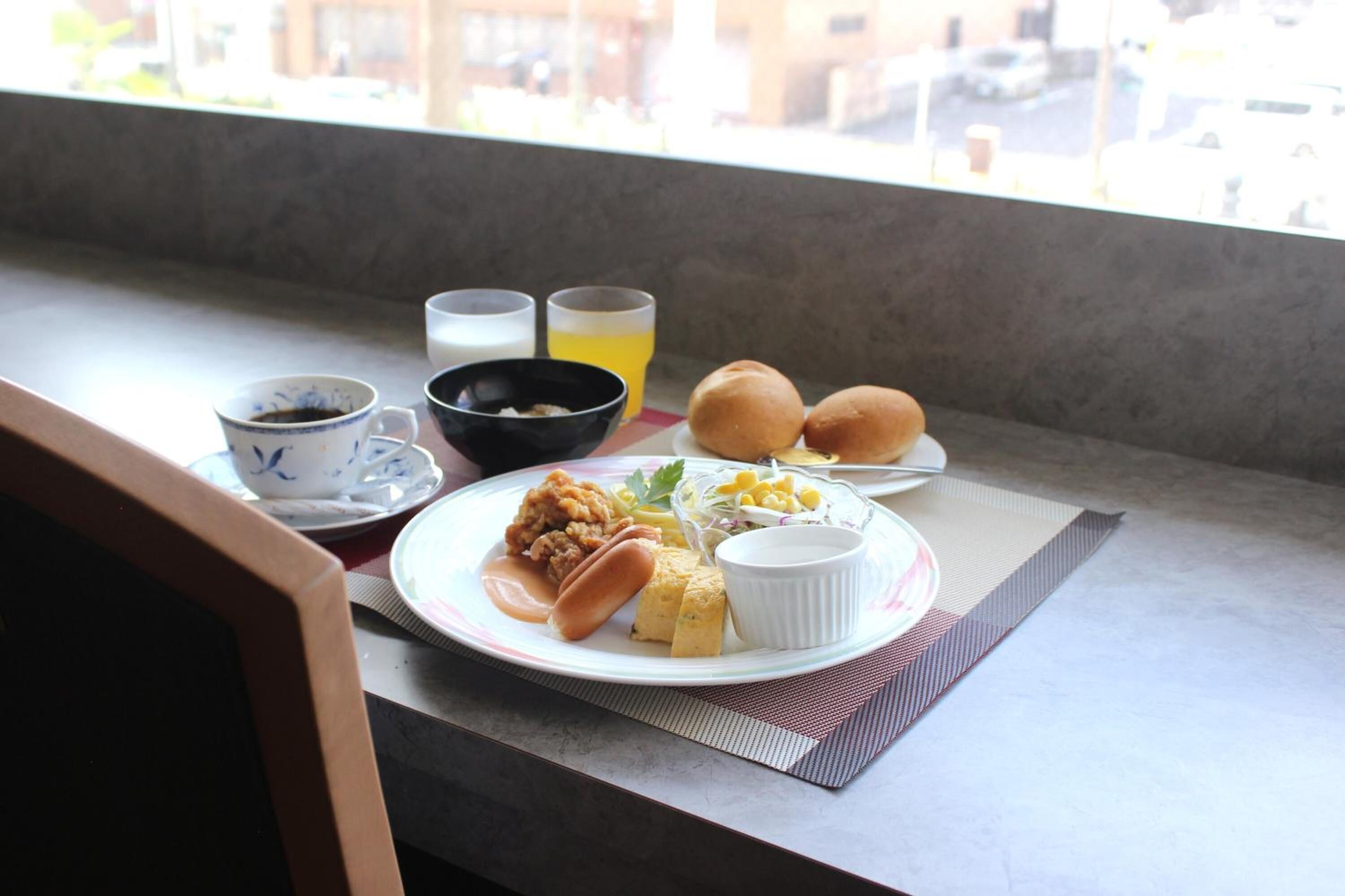 Una mesa de desayuno con un plato de comida, dos vasos de jugo de naranja, un tazón de sopa y una taza de café.