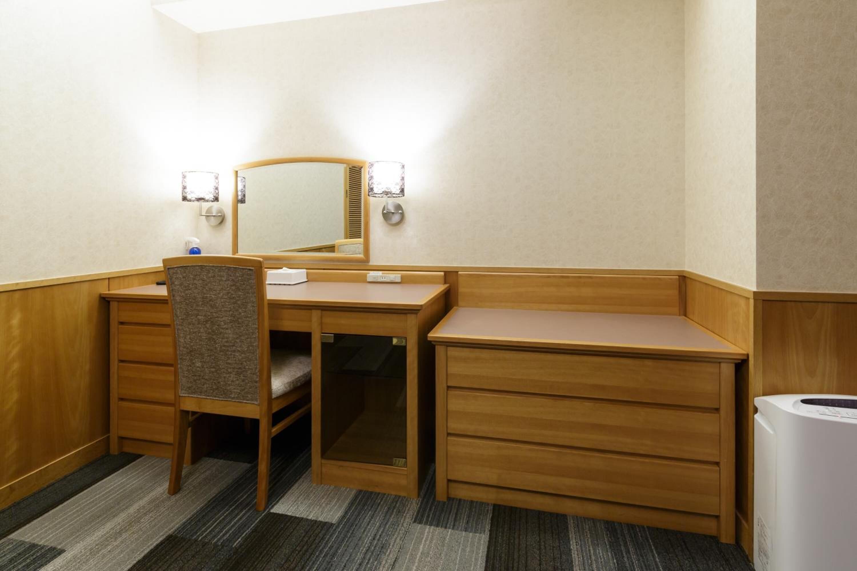 Ein Hotelzimmer mit Holztisch, einem Stuhl, einem Spiegel und einer integrierten Waschmaschine.