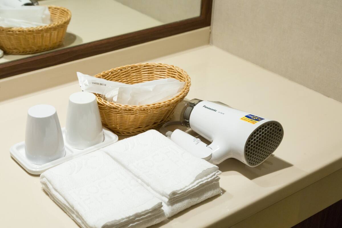 Un ripiano del bagno con un asciugacapelli, un cestino con fazzoletti e una pila di asciugamani.