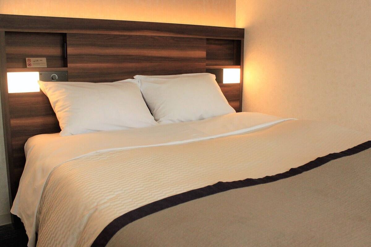 Una camera d'albergo con un letto, una testiera e due luci a parete.