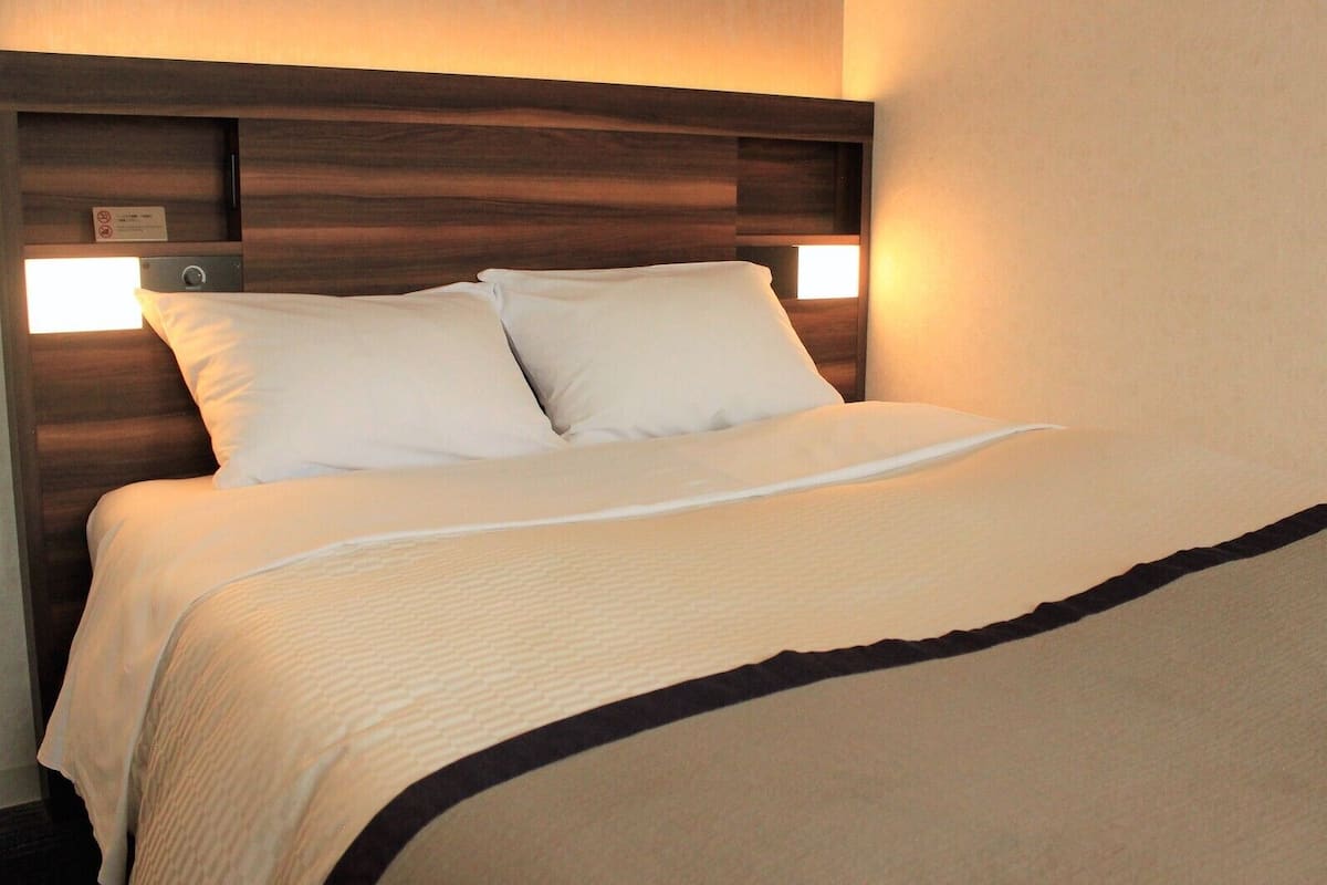 A hotel room with a bed, headboard, and two wall-mounted lights.