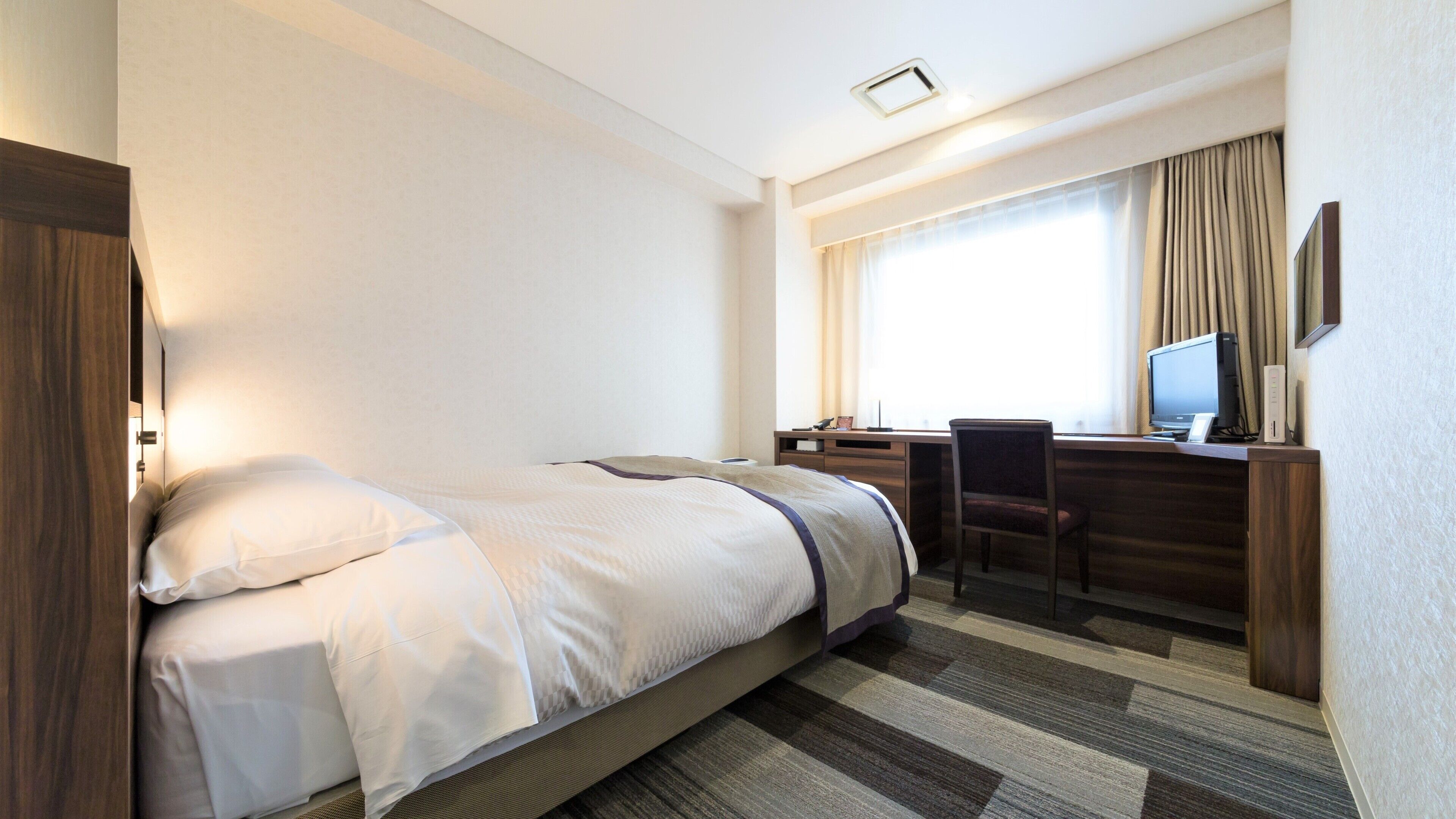 Een hotelkamer met een bed, een bureau met een computer en een stoel.