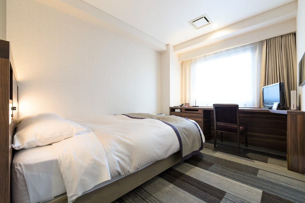 Una camera d'albergo con un letto, una scrivania con un computer e una sedia.