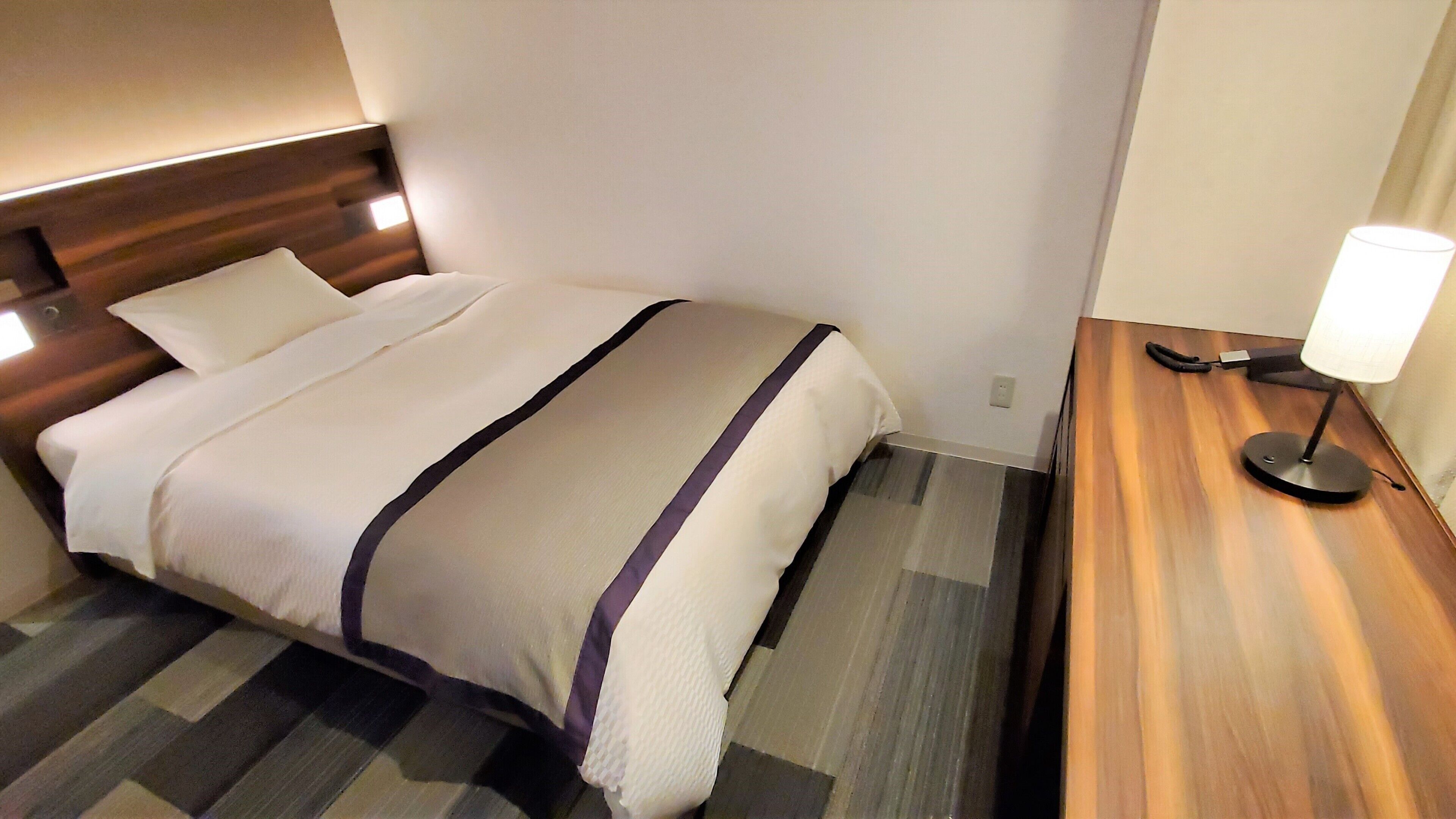 Een hotelkamer met een bed, nachtkastje, lamp en een wandlamp.
