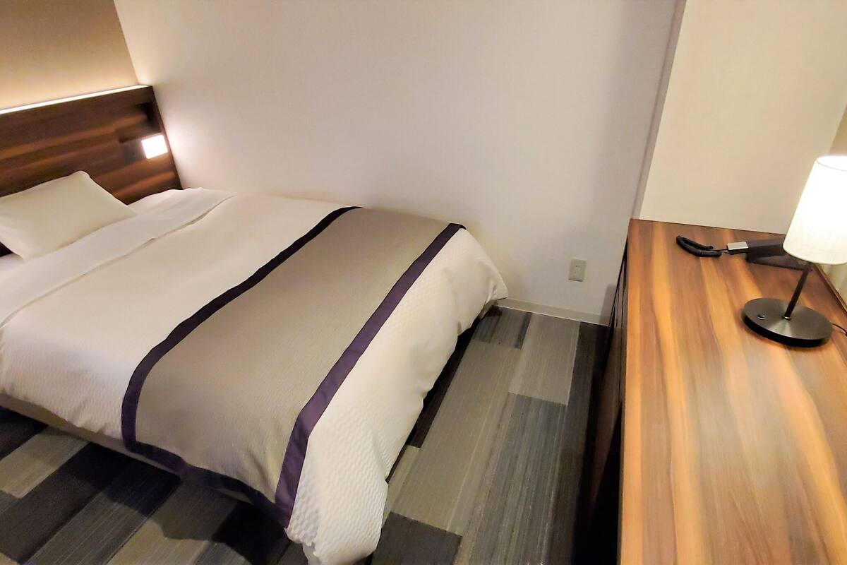 Una camera d'albergo con un letto, un comodino, una lampada e un punto luce a parete.