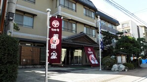 Ein traditionelles japanisches Gebäude mit einem Ziegeldach, einem hölzernen Eingang und einem roten Banner mit japanischen Schriftzeichen.