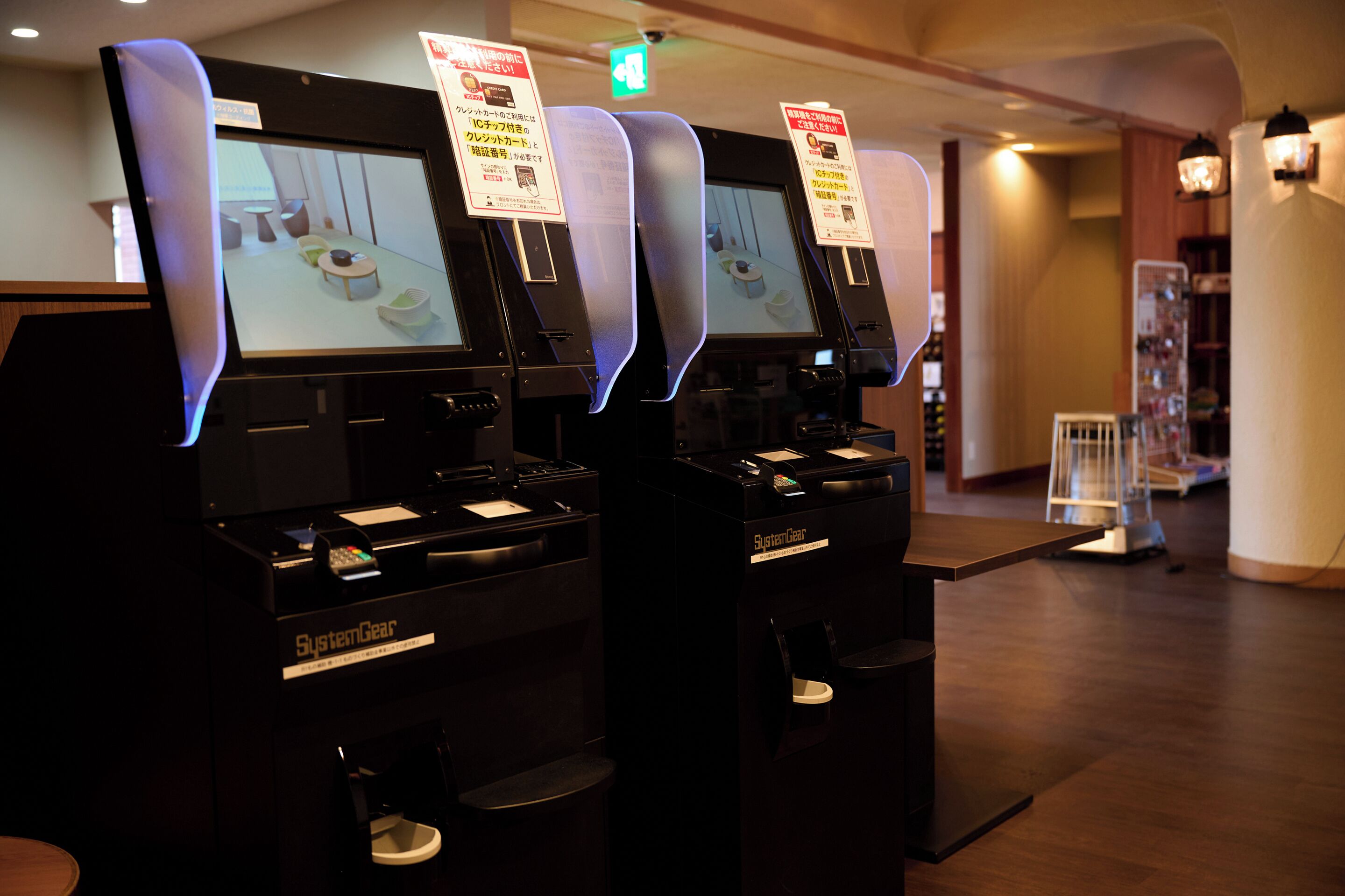 Two self-service kiosks with screens, a trash bin, and a small table with a chair.