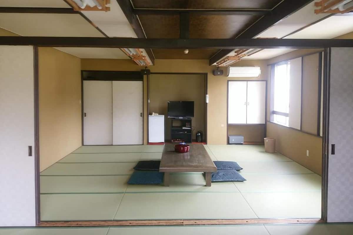 Een traditionele Japanse kamer met tatami vloerbedekking, een lage tafel, schuifdeuren en een televisie.