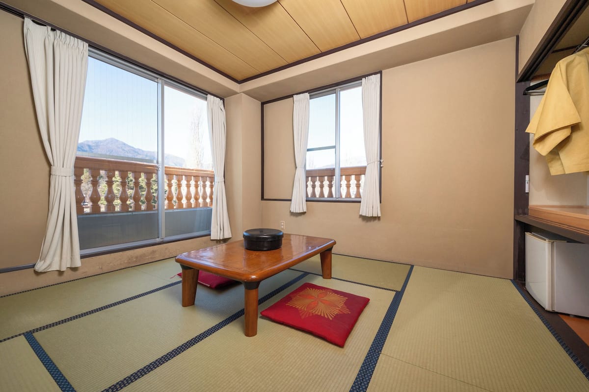 Een kamer met tatami matten, een houten tafel met een zwarte pot en een rode kussen.