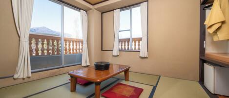 A room with tatami mats, a wooden table with a black pot, and a red cushion.