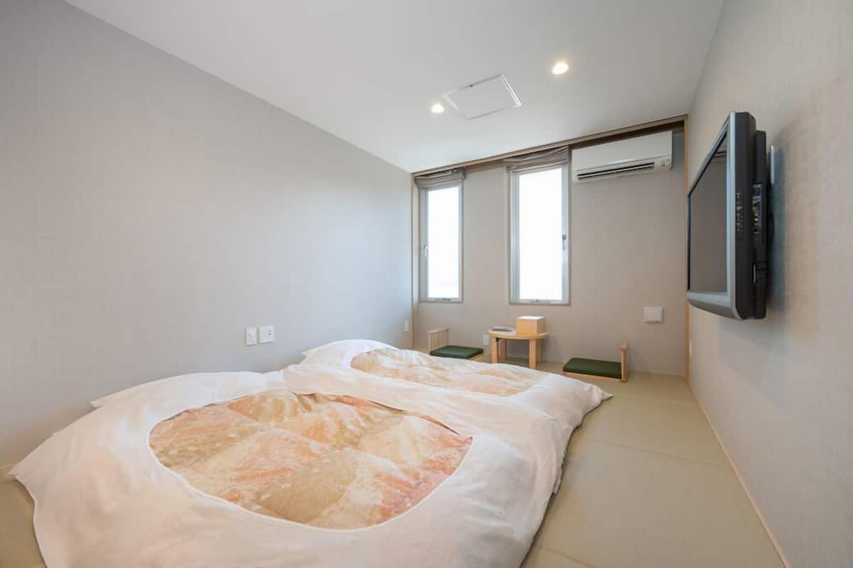 Een slaapkamer met twee bedden, een tv die aan de muur is bevestigd, en een klein tafeltje met een stoel.