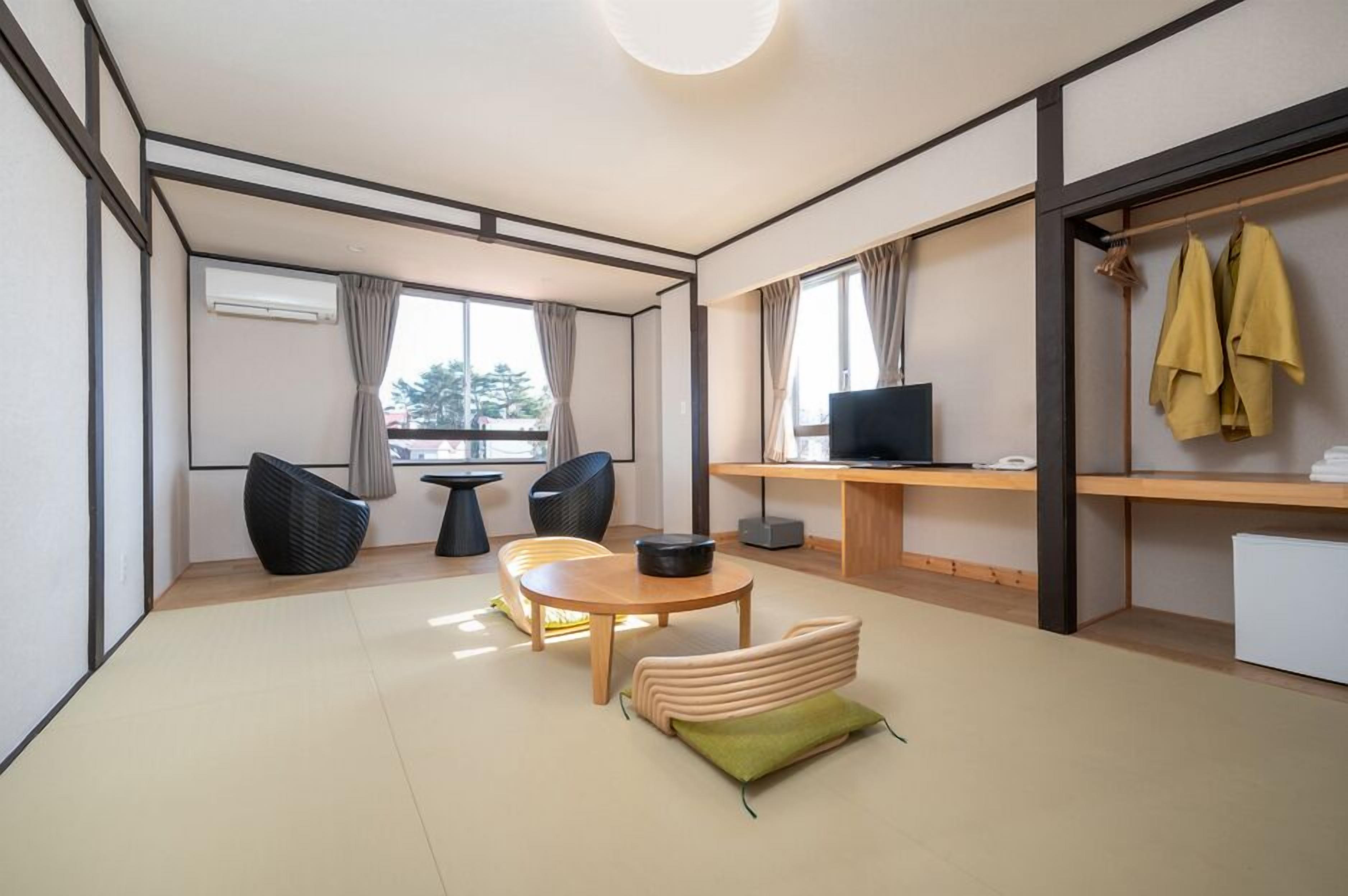 Een moderne woonkamer met een bank, stoelen, een ronde tafel, een televisie en een bureau met een computer.