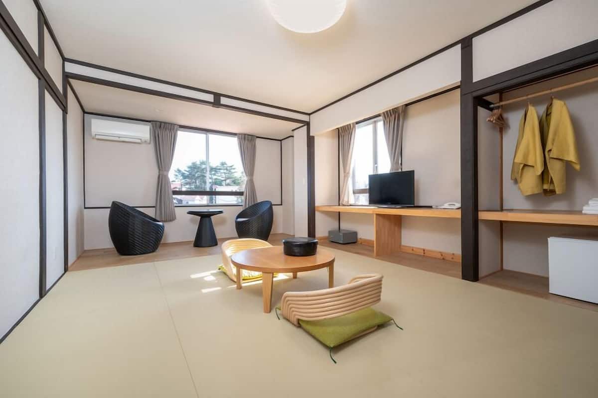 Een moderne woonkamer met een bank, stoelen, een ronde tafel, een televisie en een bureau met een computer.