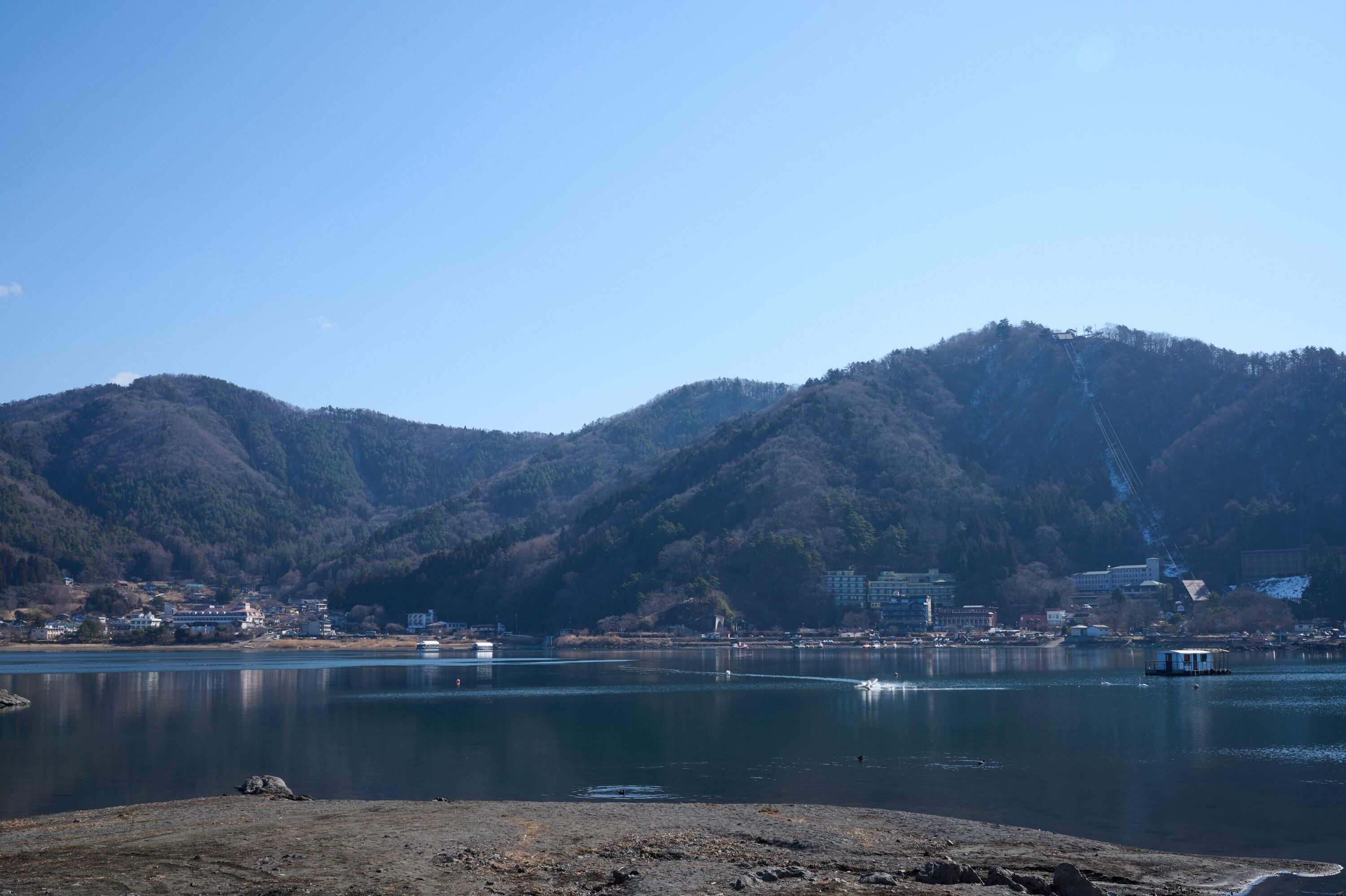 Un lago con montañas al fondo, un bote pequeño y edificios a lo largo de la orilla.