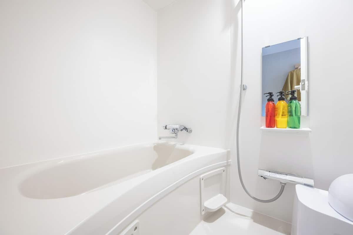 Een moderne badkamer met een witte badkuip, douche en een plank met kleurrijke flesjes.