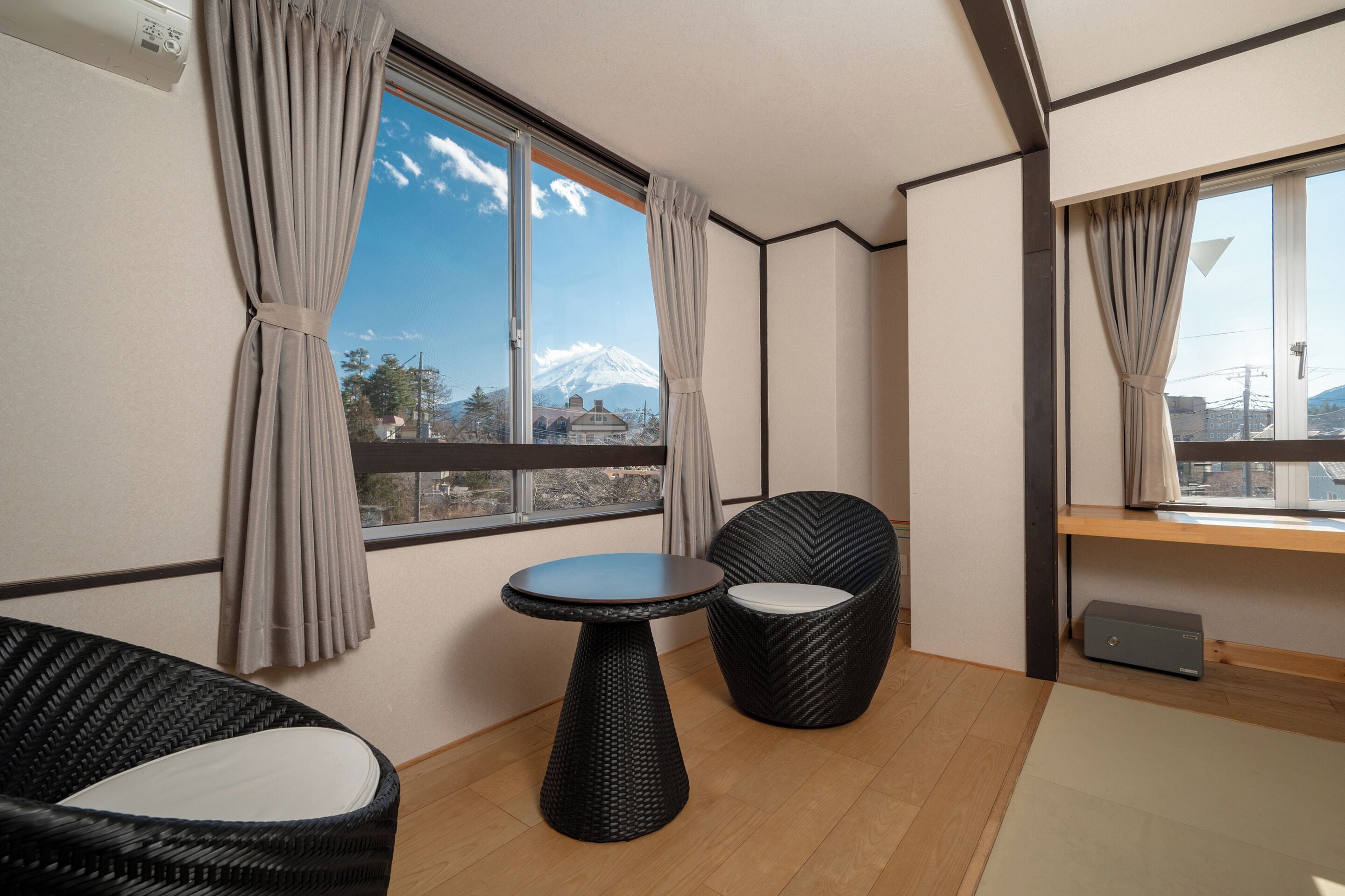 A room with a view of a mountain, a round table, two chairs, and a small shelf.