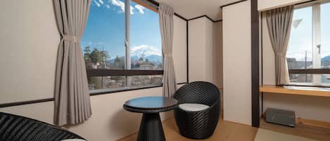 A room with a view of a mountain, a round table, two chairs, and a small shelf.