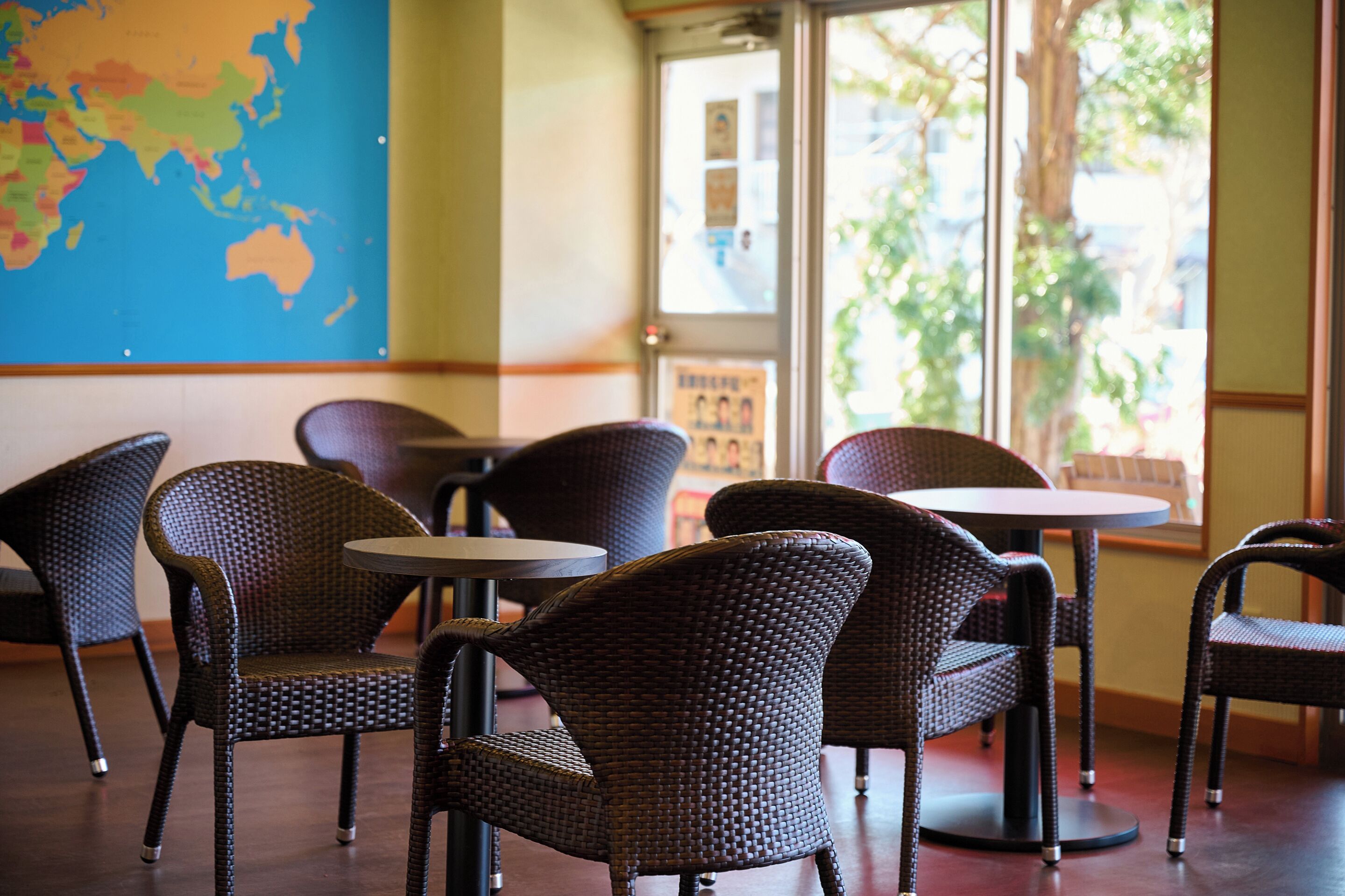 Un espace détente avec des fauteuils en osier et des tables rondes, une carte du monde accrochée au mur et une porte donnant sur l’extérieur.