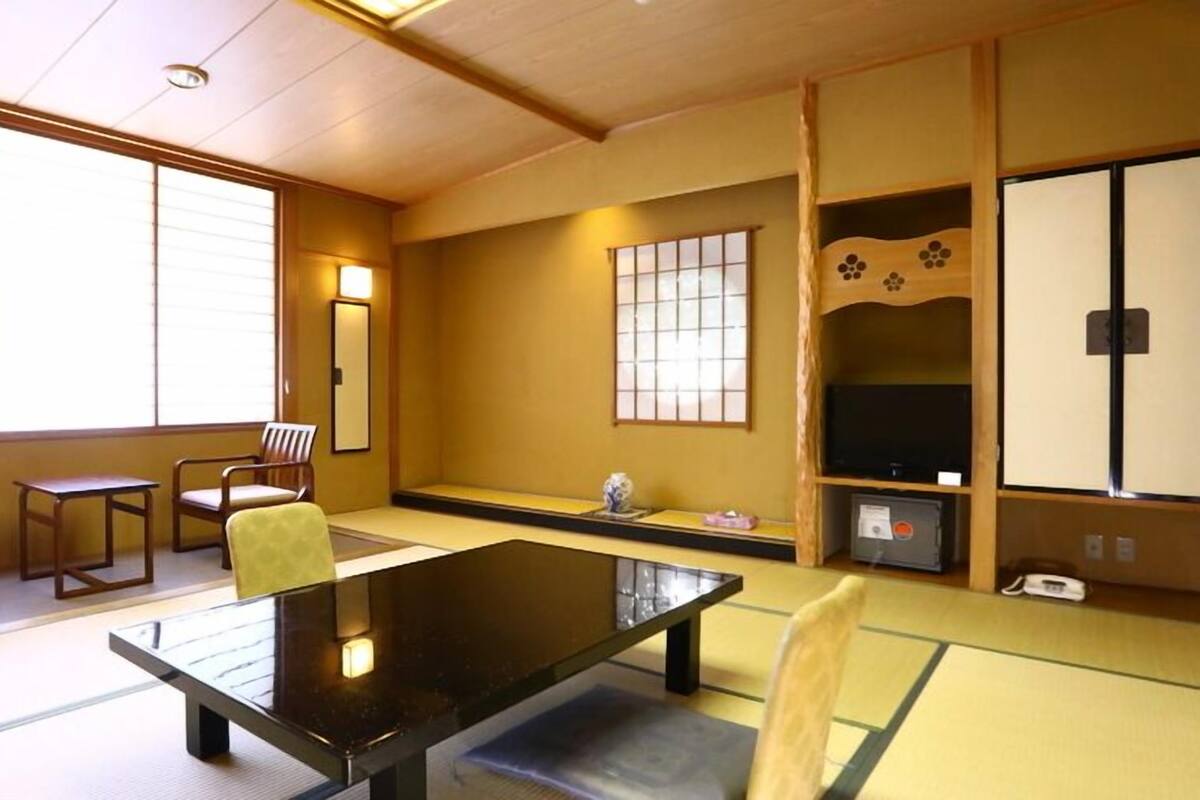 Une pièce de style japonais traditionnel, avec un sol recouvert de tatamis, une table basse, des chaises en bois, un téléviseur et des portes coulissantes.